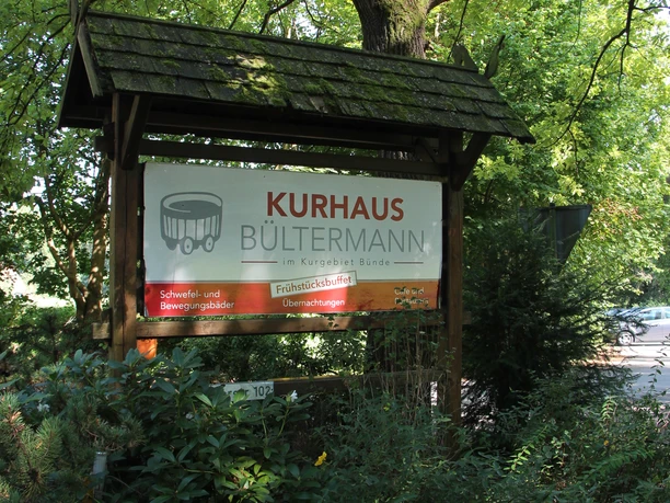 POI_1_b_Kurhaus Bültermann.JPG Ein Holzschild zwischen Bäumen weist auf das Kurhaus Bültermann im Teutoburger Wald hin.