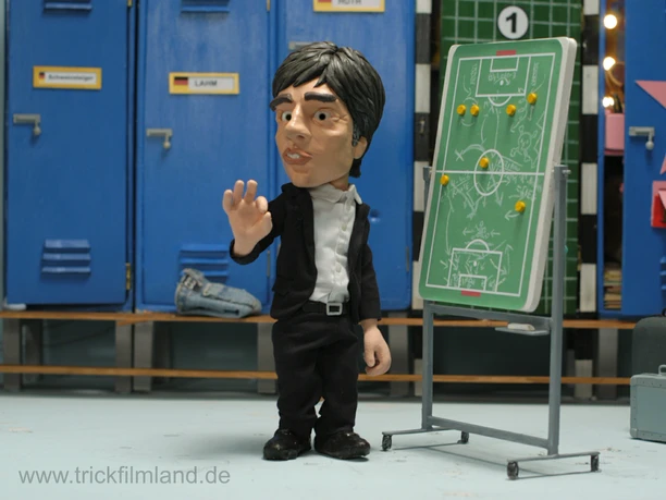Trickfilmland - Animated character football coach An animated figure stands in front of a board with a football fixture list.