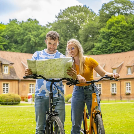 Marstall Clemenswerth, Sögel – Radfahren Hümmling ©Emsland Tourismus GmbH (2).jpg Zwei Radfahrende betrachten eine Karte vor dem historischen Marstall Clemenswerth in Sögel.