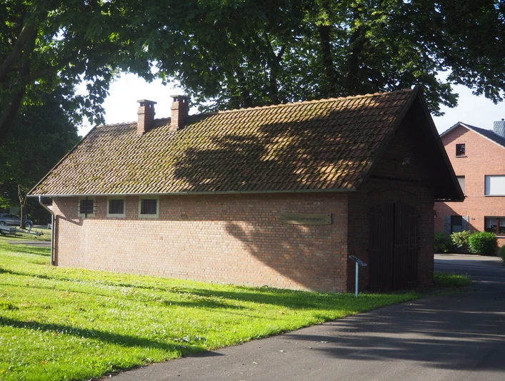 Altes Amtsgefängnis Ein kleines, altes Backsteingebäude mit schrägem, moosbewachsenem Ziegeldach. Daneben stehen grüne Bäume und das Gras leuchtet in der Sonne.