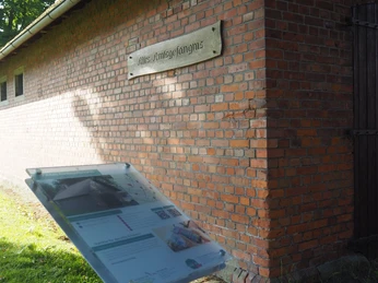 Altes Amtsgefängnis Das Bild zeigt ein altes Ziegelgebäude mit einem Schild, das die Aufschrift "Altes Amtsgefängnis" trägt. Rechts neben dem Gebäude befindet sich eine Infotafel im Vordergrund, die zusätzliche Informationen bietet.