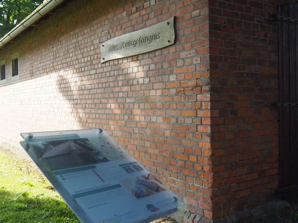 Altes Amtsgefängnis Das Bild zeigt ein altes Ziegelgebäude mit einem Schild, das die Aufschrift "Altes Amtsgefängnis" trägt. Rechts neben dem Gebäude befindet sich eine Infotafel im Vordergrund, die zusätzliche Informationen bietet.