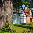 Heimatstube Südhemmern Ein Fachwerkhaus mit rotgedecktem Nebengebäude hinter einem markanten Baum an einem sonnigen Tag.
