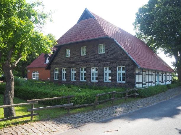 Heimatstube Südhemmern Traditionelles Fachwerkhaus mit rotem Ziegeldach, umgeben von Bäumen an einer ruhigen Straße.