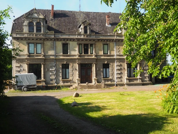 Herrenhaus Südhemmern Das Bild zeigt das historische Herrenhaus Südhemmern, flankiert von grünen Bäumen und einem gepflegten Rasen.