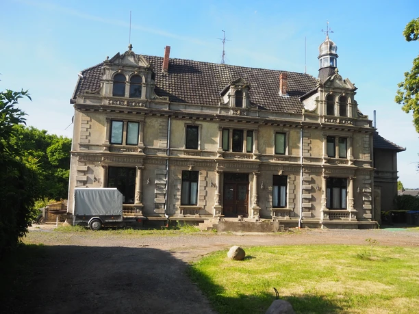 Herrenhaus Südhemmern Ein historisches Herrenhaus mit verzierten Giebeln und großen Fenstern auf einem gepflegten Grundstück.