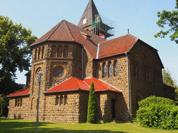 Eine majestätische Kirche aus Sandstein erscheint im Sonnenlicht. Mit rotem Ziegeldach, umgeben von grünem Rasen.