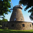 Windmühle Hartum Die Windmühle Hartum, eine historische Mühle aus Naturstein, steht majestätisch in einer grünen Wiese, eingerahmt von Bäumen. Sie ist ein beeindruckendes Beispiel traditioneller Handwerkskunst und bietet einen nostalgischen Anblick in der sommerlichen Idylle. Ihre markanten Flügel und der zylindrische Turm aus Bruchstein verleihen ihr eine elegante Robustheit.