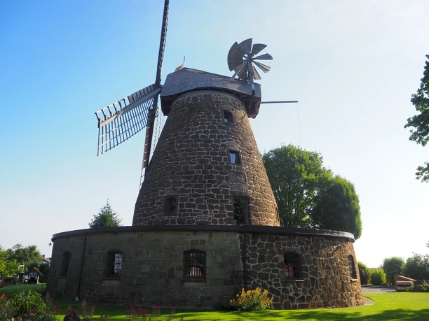 Windmühle Hartum im Sonnenschein, mit robustem Steinbau, stilvollen Flügeln und umgeben von grüner Natur.