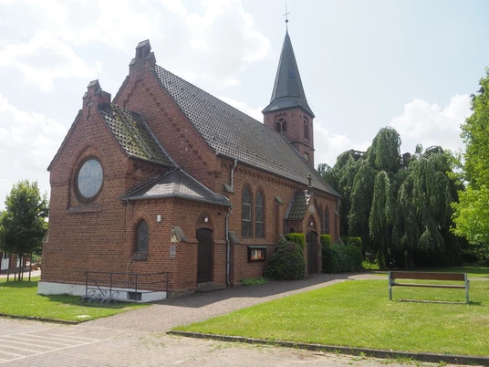 Christuskirche Oberbauerschaft Die Christuskirche Oberbauerschaft ist ein Backsteingebäude mit einem hohen Turm und großen Buntglasfenstern, umgeben von gepflegtem Rasen und Bäumen.