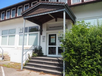 Eingang des Heimatmuseums Hüllhorst mit überdachtem Treppenaufgang und grüner Bepflanzung.