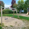 Spielplatz Gabelhorst 29 Ein kleiner Sandspielplatz mit zwei Schaukeln, Rutsche und Klettergerüst, umgeben von Grün.