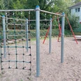 Spielplatz Graudenzer Weg Es gibt ein Bild von einem Spielplatz zu beschreiben. Hier ist der barrierefreie Beschreibungstext:Spielplatz auf Sandboden mit Kletternetz, Kletterstangen und Schaukel im Hintergrund, umgeben von Bäumen und Wohngebäuden.