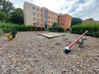 Spielplatz Habelschwerdter Hof Ein moderner Spielplatz umgeben von Wohngebäuden. Sichtbar sind Schaukeln, ein Wipptier und eine Wippe.