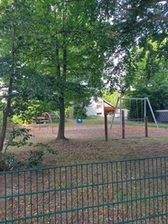 Ein Spielplatz mit Metallgeräten auf Rindenmulch, umgeben von großen Bäumen, lädt zum Toben ein.