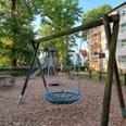 Spielplatz Isenstedter Straße Ein lebendiger Spielplatz mit Wippe, Schaukeln und Rutsche, umgeben von Bäumen und Wohnhäusern.