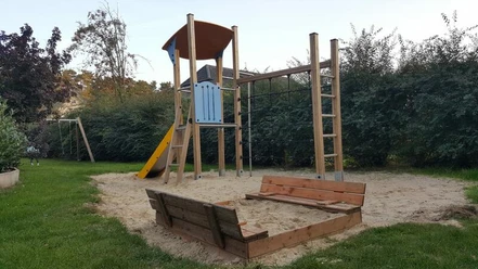 Spielplatz Koloniestraße Der Spielplatz an der Koloniestraße ist mit einem Kletterturm und einer Rutsche ausgestattet, umgeben von grünem Rasen und Hecken, was eine freundliche Spielatmosphäre schafft.