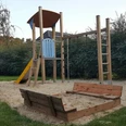 Spielplatz Koloniestraße Der Spielplatz an der Koloniestraße ist mit einem Kletterturm und einer Rutsche ausgestattet, umgeben von grünem Rasen und Hecken, was eine freundliche Spielatmosphäre schafft.