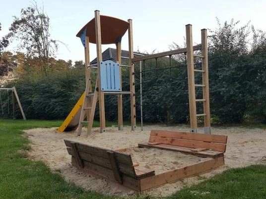 Spielplatz Koloniestraße Der Spielplatz an der Koloniestraße ist mit einem Kletterturm und einer Rutsche ausgestattet, umgeben von grünem Rasen und Hecken, was eine freundliche Spielatmosphäre schafft.