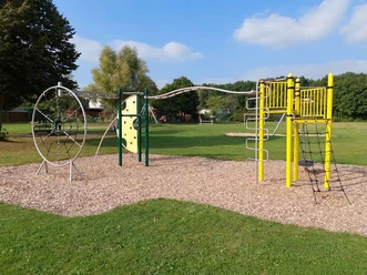 Ein moderner Spielplatz umfasst eine Kletterstruktur mit Netzen und Leitern auf Rindenmulch.