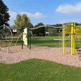 Ein moderner Spielplatz umfasst eine Kletterstruktur mit Netzen und Leitern auf Rindenmulch.
