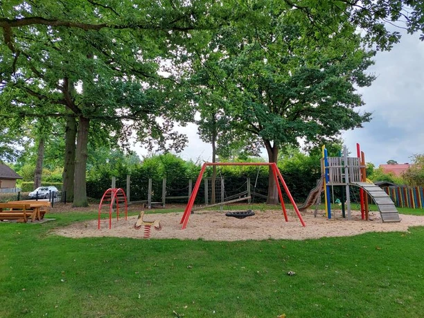 Spielplatz Lauenburger Straße Spielplatz mit Rutsche, Klettergerüst und Schaukeln, umgeben von grünem Rasen und Bäumen.