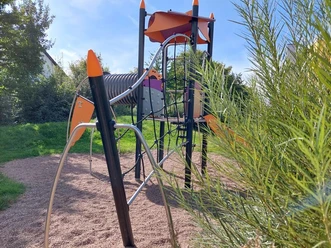 Modern gestalteter Spielplatz mit Klettergerüst in leuchtenden Farben, umgeben von Grünfläche.