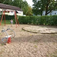 Spielplatz Preußeneck Der Spielplatz am Preußeneck zeigt Schaukel und Federtier auf sandigem Boden, umgeben von grüner Hecke.