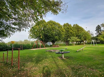 Ein idyllischer Spielplatz mit Schaukel, Wippe und Schaukeltischen, umgeben von üppigem Grün.