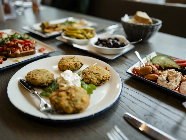 Stadtführungen © Matheus Fernandes (88).jpg Teller mit frittierten Gemüsepatties und Dips, umgeben von verschiedenen Antipasti auf Holztisch.
