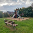 Spielplatz Röthenstraße Ein Spielplatz mit einer bunten Rutsche und Schaukel, umgeben von Bäumen unter einem bewölkten Himmel. Eine Holzbank steht auf einer Wiese.