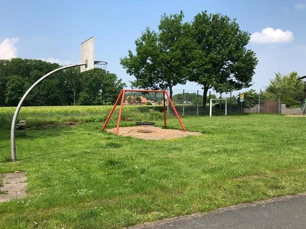 Spielplatz Am grünen Kranze Spielplatz mit Basketballkorb, einer Schaukel, umgeben von grüner Landschaft und Bäumen.