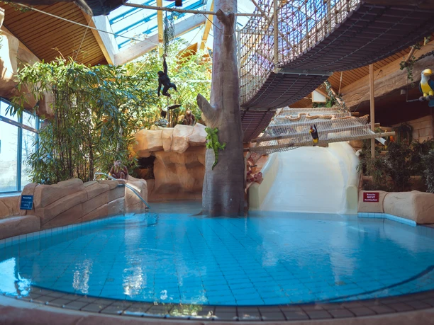 Ein Innenpool mit Rutsche im H2O Freizeitbad Herford, umgeben von tropischen Pflanzen.