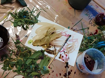Naturfarbenwerkstatt.jpg Künstlerische Materialien und natürliche Elemente wie Blätter und Pigmente auf einem Arbeitstisch verteilt.