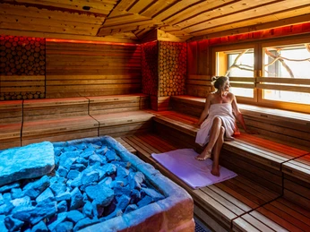 Eine Frau sitzt entspannt in einer hölzernen Sauna mit blau beleuchteten Steinen und genießt die Ruhe.