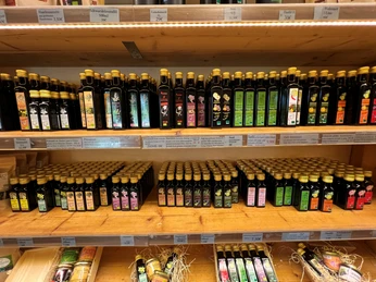 Wesermühle GbR Flaschen mit verschiedenem regionalen Öl auf Holzregalen in einem Laden. Bunte Etiketten sind sichtbar.