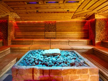 Eine moderne Sauna mit Holzwänden und einem zentralen Steinhaufen für Aufgüsse, in warmem Licht.