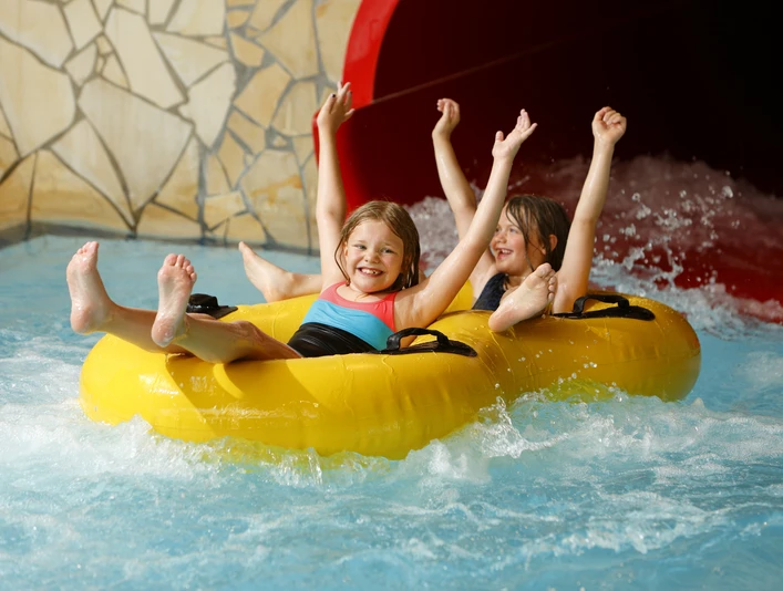 Zwei lachende Kinder rutschen in gelben Reifen voller Freude eine Wasserrutsche hinunter.