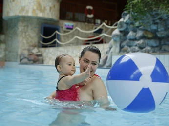 Eine Mutter und ihr Kind spielen im Wasser eines Hallenbads mit einem bunten Wasserball.