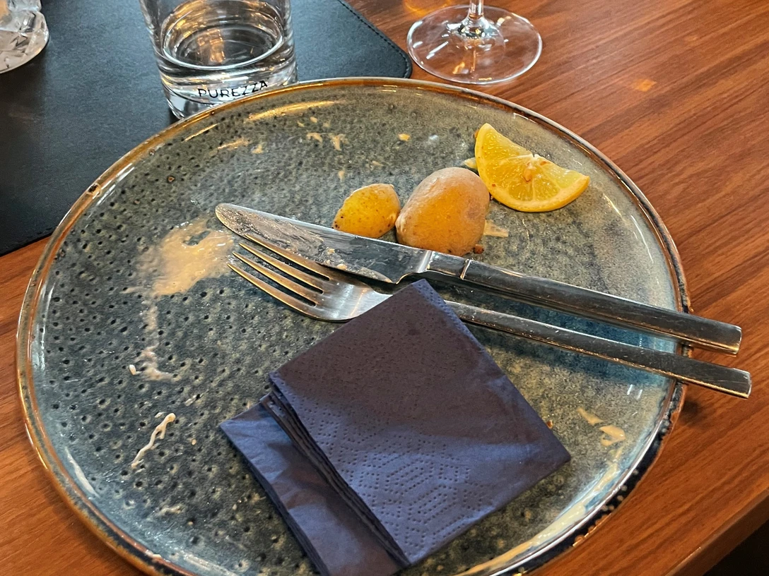 Aufgegessen, war lecker!-Platzhalterbild.jpg Leerer Teller mit Messer, Gabel, zwei Kartoffeln und Zitronenscheibe, daneben ein Wasserglas.