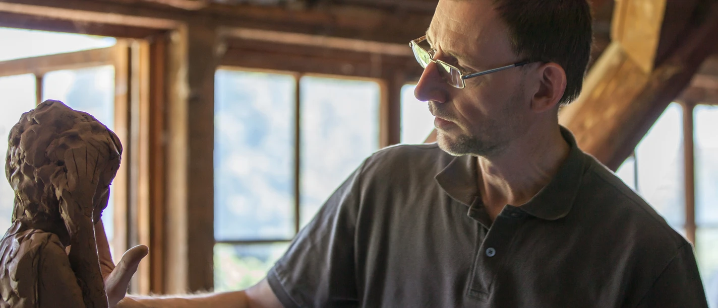 4.21_Bildhauer Thorsten Held_LandArt-Station 4.21.jpg Der Bildhauer Thorsten Held arbeitet konzentriert an einer Tonfigur in einem lichtdurchfluteten Atelier.