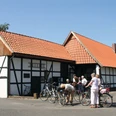 Alte Schule Wietersheim_Radfahrergruppe am Fachwerkhaus.jpg Eine Gruppe von Radfahrern pausiert vor einem traditionellen Fachwerkhaus unter klarem Himmel.