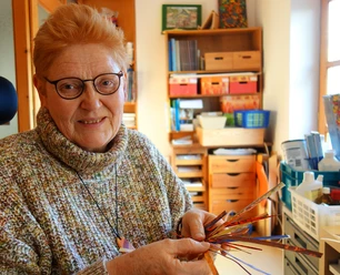 4.28_Kuenstlerin_Bettina Bollmann-Koch QUERformat_Bettina Bollmann-Koch.JPG Künstlerin Bettina Bollmann-Koch im Atelier, lächelnd mit selbst gestalteten Papierstreifen.