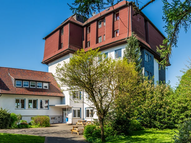 Gästehaus Mehrstöckiges Gebäude mit rotem Dach und weißen Wänden, umgeben von grünen Bäumen und Rasenflächen.