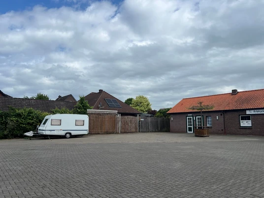 Wohnmobilstellplatz Schützenplatz2.jpg Ein Wohnmobil steht allein auf einem großen, gepflasterten Platz, neben einem Backsteingebäude mit rotem Dach.