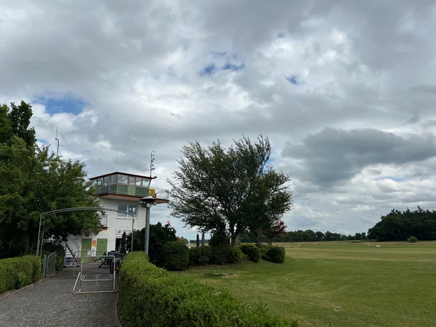 Bild2.jpg Tower für die Flugzeuge am Rande der Flugbahn zwischen Bäume. Davor ist ein Fahrradständer zu sehen.