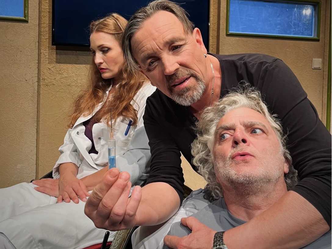 5MB©BKT.png Ein Mann zeigt einer nachdenklichen Frau einen Gegenstand, während ein anderer Mann besorgt schaut.