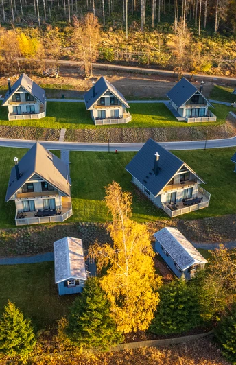 Die Luftaufnahme der Harz-Urlaubs-Alm in Buntenbock zeigt gemütliche Ferienhäuser auf grünen Wiesen, umgeben von bunten Herbstbäumen im Harz.