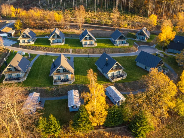 Die Luftaufnahme der Harz-Urlaubs-Alm in Buntenbock zeigt gemütliche Ferienhäuser auf grünen Wiesen, umgeben von bunten Herbstbäumen im Harz.