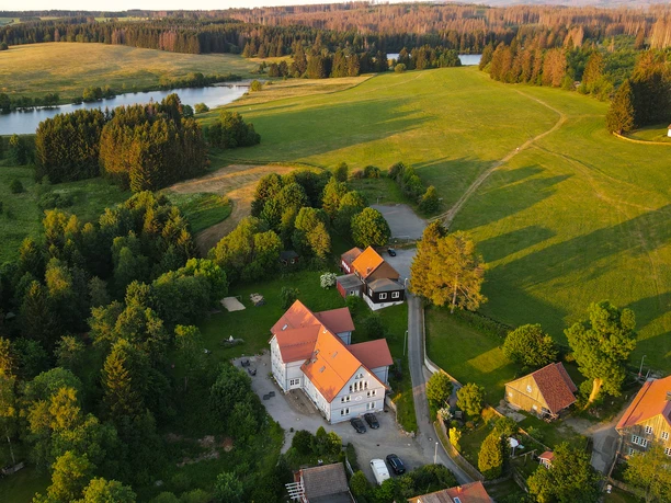 Die Luftaufnahme zeigt das idyllisch gelegene Hotel Urlaubs-Alm Buntenbock im Harz, umgeben von saftigem Grün und einem Teich. Ein perfekter Rückzugsort inmitten der Natur.